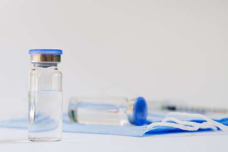 Creative ideas of vaccination concept. Top view of syringe with medical masks and vaccine vial glass bottles for vaccination against COVID-19. Coronavirus pandemic. Copy space.の写真素材