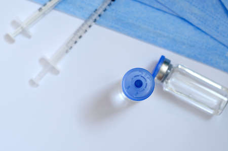Creative ideas of vaccination concept. Top view of syringe with medical masks and vaccine vial glass bottles for vaccination against COVID-19. Coronavirus pandemic. Copy space.の写真素材