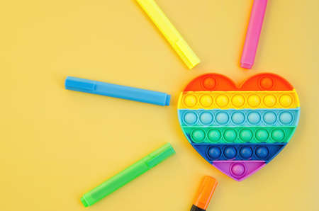Top view of colorful markers and anti stress sensory toy   rainbow heart on yellow background close up. Creative and funny concepts of children toys. Popular toy. Trend toy 2021 year.の写真素材