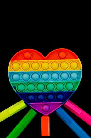 Top view of colorful anti stress sensory toy pop it rainbow heart on black background close up. And...