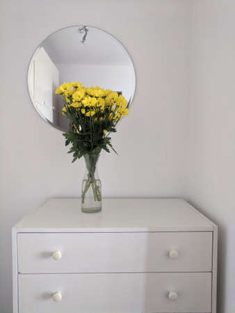 A minimalist bedroom interior, a guest room with a round mirror, white chest of drawers with yellow...