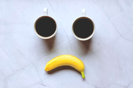 Businessman working morning with cups of hot black coffee and yellow banana on white background. Top...