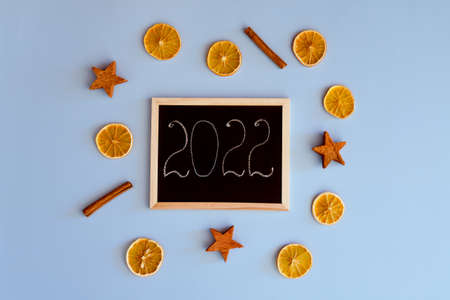 Christmas, New Year flat lay on blue background with place for text. Christmas decorations with dry spices, orange rings and cinnamon. numbers 2022 on a writing board. Top view. Copy space. Mock up.の写真素材