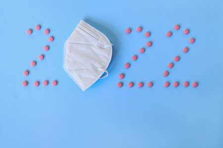 Christmas, New Year flat lay on blue background. numbers 2022 making with pills and medical mask....