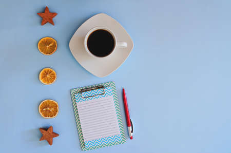 Christmas, New Year flat lay on blue background. Christmas decorations with dry spices, orange rings, cinnamon. Cup of hot black coffee. writing board, notebook paper. Top view. Copy space. Mock upの写真素材