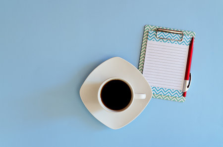 flat lay on blue background. Cup of hot black coffee. Notebook paper, pen. Top view. Copy space....