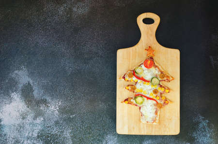 Delicious vegetarian Christmas tree pizza with tomatoes, vegetables and cheese on black background. Creative, funny food concept for kids. Top view, flat lay. Copy space.の写真素材