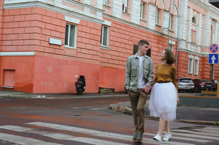 Kharkiv, Ukraine. 09.19.2021. Love story of stylish funny couple: young man in a t-shirt. And a cute young woman in wedding white skirt and yellow sweater. Family holiday and togetherness, dateのeditorial素材