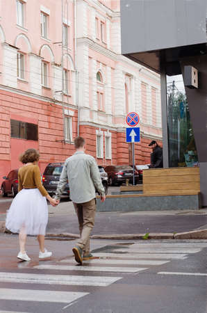 Kharkiv, Ukraine. 09.19.2021. Love story of stylish funny couple: young man in a t-shirt. And a cute young woman in wedding white skirt and yellow sweater. Family holiday and togetherness, dateのeditorial素材