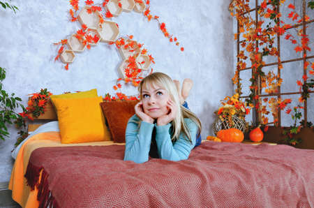 A young cute blonde woman in yellow sweater sits on window seat in cozy home with autumn festive...