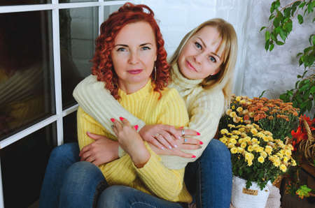 Two lovely young women, sisters, friends in warm sweaters are sitting in the bed at a cozy home,...