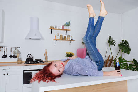 Young cute redhead curly woman 30+ in blue jeans and a shirt sitting and relaxing in her bright...