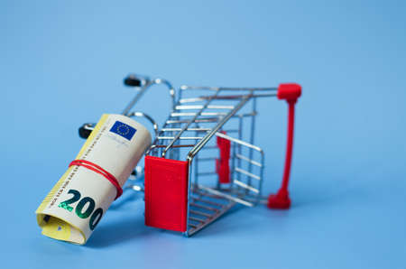 Mini shopping grocery push cart with euro banknotes, money on blue background. Business, finance concept. Concept of shopping. Economy concept.の写真素材