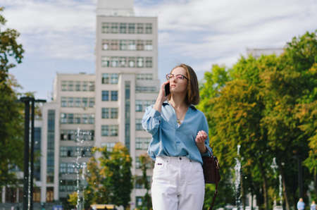 Urban portrait of young elegant business woman in eye glasses and casual clothes. Woman walking in...