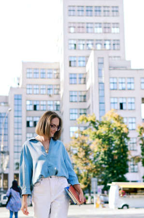 Urban portrait of young elegant business woman in eye glasses and casual clothes in city. Woman walking in green park, relaxing, smiling in sunny day. Hobby and leisure.の写真素材