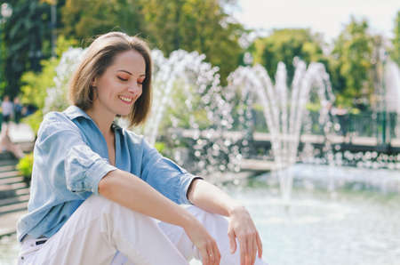 Urban portrait of young elegant business woman in eye glasses and casual clothes in city. Woman walking in green park, relaxing, smiling in sunny day. Hobby and leisure.の写真素材