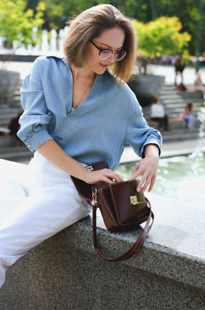 Urban portrait of young elegant business woman in eye glasses and casual clothes in city. Woman walking in green park, relaxing, smiling in sunny day. Hobby and leisure.の写真素材