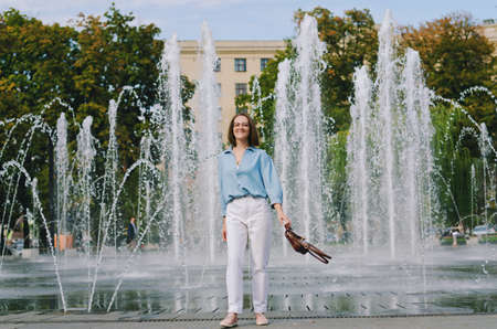 Urban portrait of young elegant business woman in eye glasses and casual clothes in city. Woman walking in green park, relaxing, smiling in sunny day. Hobby and leisure.の写真素材