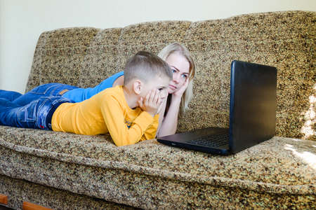 Mother and small child, boy at home sitting on couch, using laptop, relax. Working from home. Happy...