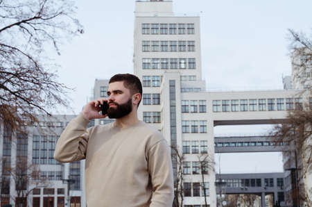 Urban portrait of young elegant business man in winter casual clothes, jacket, hat. Walking in the city street, talking on the phone, making selfie. working outdoor.の写真素材