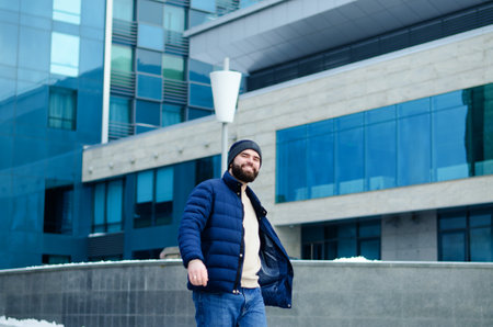 Urban portrait of young elegant business man in winter casual clothes, jacket, hat. Walking in the city street, talking on the phone, making selfie. working outdoor.の写真素材