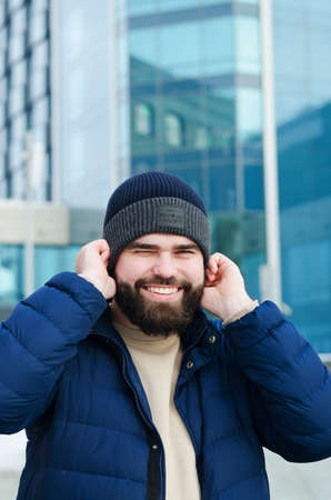 Urban portrait of young elegant business man in winter casual clothes, jacket, hat. Walking in the city street, talking on the phone, making selfie. working outdoor.の写真素材