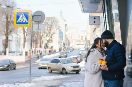 Couple in love kissing and drinking coffee on the street. Man and woman in winter clothes on the...