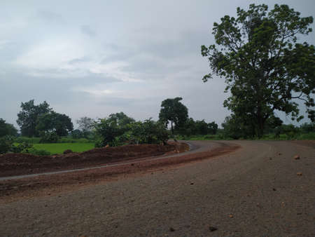 Countryside road between farms under cloudy sky in monsoon