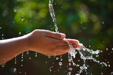 Water pouring in kid two hand on nature background. Hands with water splash.の写真素材