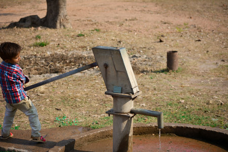TIKAMGARH, MADHYA PRADESH, INDIA - NOVEMBER 20, 2019: Unidentified indian village little boy pumping hand water pump.のeditorial素材