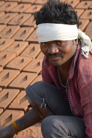 TIKAMGARH, MADHYA PRADESH, INDIA - FEBRUARY 07, 2020: Unidentified Indian man making house bricks by hand using a mold and wet clay.のeditorial素材