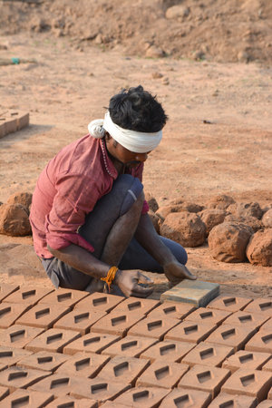TIKAMGARH, MADHYA PRADESH, INDIA - FEBRUARY 07, 2020: Unidentified Indian man making house bricks by hand using a mold and wet clay.のeditorial素材