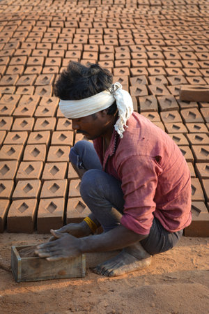 TIKAMGARH, MADHYA PRADESH, INDIA - FEBRUARY 07, 2020: Unidentified Indian man making house bricks by hand using a mold and wet clay.のeditorial素材