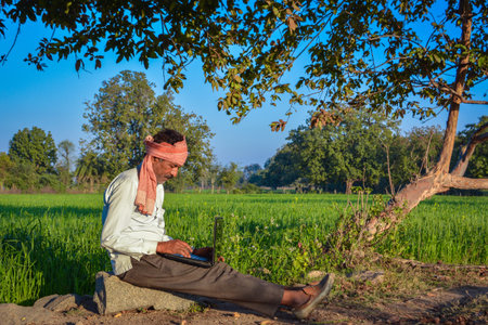 Indian rural man using laptop at agriculture field. Modern technology in agriculture