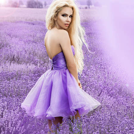 Beautiful model walking in spring or summer lavender field in sunrise. Blond long haired girl in lavender field - Imageの写真素材