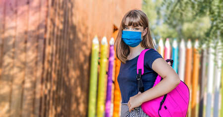 Schoolgirl wearing face mask during epidemic. Back to school concept. Cute girl outside at school. Safety mask to coronavirus prevention. Kid with backpack going to school. Education.の写真素材
