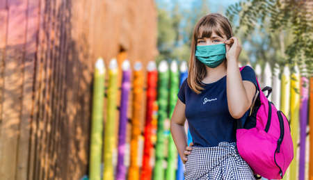 Schoolgirl wearing face mask during epidemic. Back to school concept. Cute girl outside at school. Safety mask to coronavirus prevention. Kid with backpack going to school. Education.の写真素材