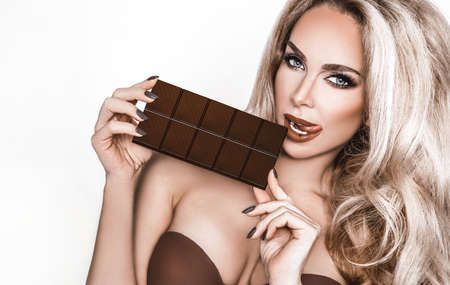Portrait of a satisfied pretty girl biting chocolate bar and looking at camera isolated over white...