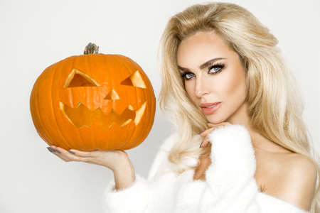 Beautiful young woman in white sweater, standing on white background and holding pumpkin;の写真素材