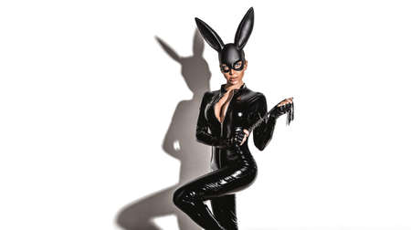 Halloween sexy girl in bunny costume. Sexy blonde beautiful woman posing in latex costume and black bunny mask on white background. Hallooween concept.の写真素材