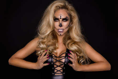 Sexy blonde woman in Halloween makeup and leather outfit on a black background in the studio....