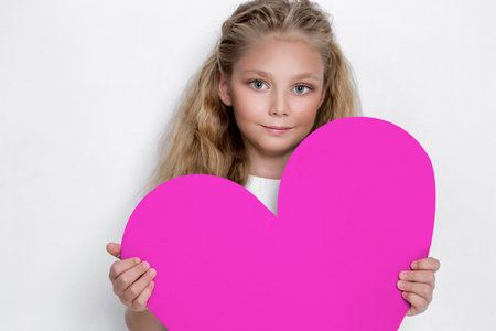 Pretty little girl holds a heart in his hands and standing on a white background.の写真素材