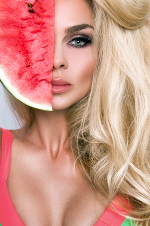 Beautiful female model with long blond hair, holding a watermelon at her face. Watermelon concept.の写真素材
