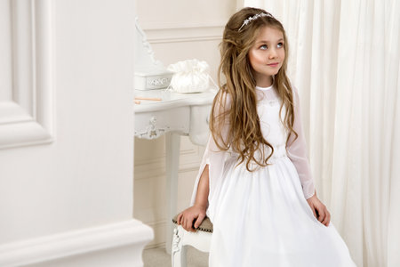 Little girl in white communion dress. First holy communion - concept. Young model in the white communion dress stands in an elegant palace.の写真素材