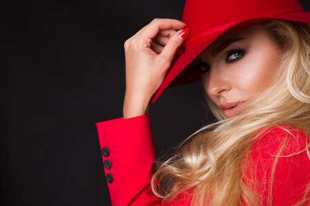 Beautiful blonde woman in a red hat, red jacket suit on a black background. Elegant stylish concept.の写真素材