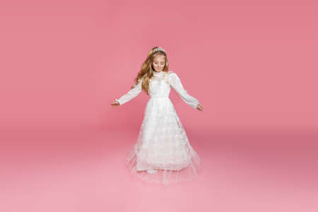 Little girl in white communion dress. First holy communion - concept. Young model in the white communion dress isolated on pink background.の写真素材