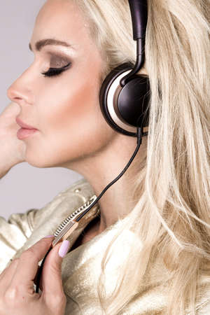 Beautiful young woman listening to music on headphones. Elegant style, music. Pretty girl listening music with her headphones in studio.の写真素材