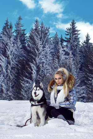 Beautiful young woman with Husky dog. Winter fashion. Snow, mountains and winter vacations.