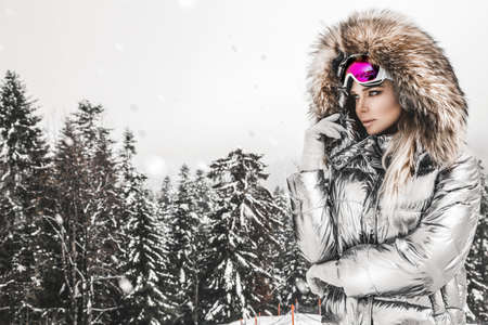 Young woman winter portrait. Winter fashion model with ski suit and goggles. Attractive young woman in wintertime outdoor. Mountains, white snow in magic winter day.の写真素材