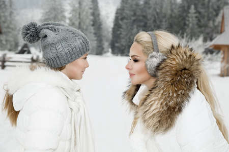 Winter family time. Beautiful woman with kid in winter day. Mother and daughterb in winter clothes on mountains background.の写真素材